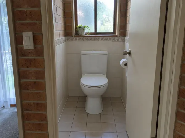Clean toilet in a tiled small bathroom with brick walls and a window in Cromer