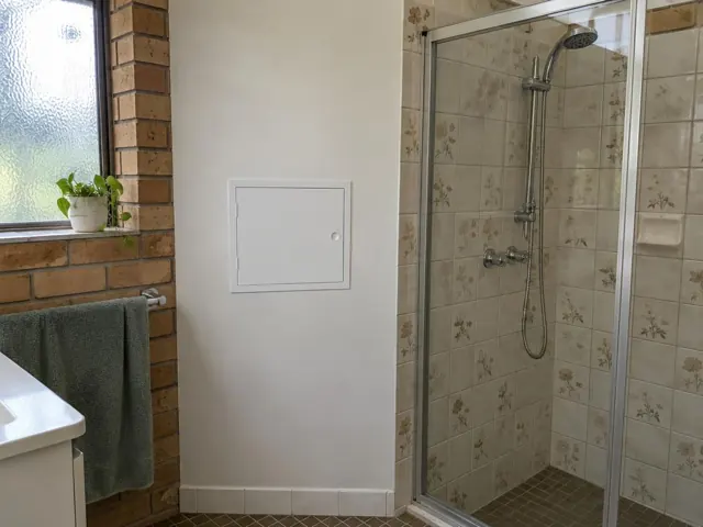Bathroom wall with a small square access panel beside a shower and tiled brick wall in Dee Why