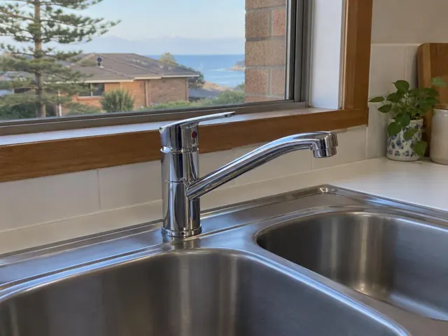 Chrome kitchen mixer tap over a double stainless sink with tiled splashback and timber window frame in Collaroy